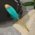 Elegante penna a sfera in piuma turchese e oro su una pagina di libro vintage per regali creativi - Ciano