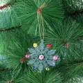 Transparent snowflake Christmas ornament with colorful beads on a green pine tree background. - Blue