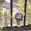 Close-up of a purple faux peony flower in a white pot on a bright, sunny windowsill. - Peony Style / Purple Peony