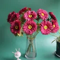 Detailed view of artificial magenta gerbera daisies in a gold-rimmed glass vase. - Rose Red
