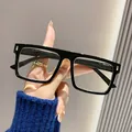 Gedetailleerde close-up van een hand die een moderne zwarte vierkante leesbril houdt - +1.00 Dioptrie / Zwart