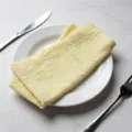 Soft textured light yellow cotton table napkin with raw fringe edges on a ceramic plate - 32x32cm / Light Yellow