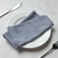 Dusty blue slub cotton cloth napkin with rustic frayed edges on a white dinner plate - 32x32cm / Grey Blue