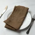 Rustic brown cotton cloth napkin with frayed edges on white plate - 32x32cm / Brown