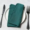 Dark green slub cotton napkin with hemmed edges on a white plate with cutlery. - 32x32cm / Dark Green