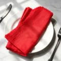 Vibrant red cotton slub cloth napkin with fringed edges folded nicely on a white plate - 32x32cm (1 Piece) / Bright Red (CD260703-1)