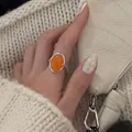 Detailansicht eines orangefarbenen ovalen Edelsteinrings an einer Hand mit Strickpullover. - Lebendiges Orange (J9472)