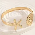 Dettaglio di bracciale rigido dorato con ciondoli stella marina e conchiglia elegante. - stella marina e conchiglia