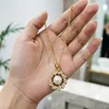Dettaglio di una collana con ciondolo a fiore dorato con perla centrale e strass - Collana