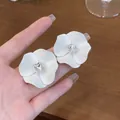 Primo piano di eleganti orecchini a fiore bianco opaco con zircone quadrato centrale - Bianco