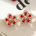 Detailed shot of gold-toned flower stud earrings with red and clear zircon stones. - Red