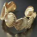 Dettaglio di un elegante bracciale rigido dorato con motivo a conchiglia e finitura lucida - Capasanta
