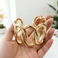 Primo piano di un bracciale a polsino in oro a maglie grandi, finitura lucida oro. - Cerchi collegati