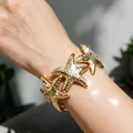 Vista dettagliata di un elegante bracciale largo regolabile con stelle marine d'oro su un polso - A stella