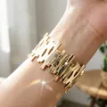 Dettaglio ravvicinato del bracciale aperto geometrico dorato testurizzato sul polso - Consistenza della Corteccia Irregolare