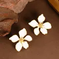 Eleganti orecchini a fiore in smalto bianco con bordi dorati in un primo piano. - Bianco