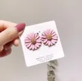 Detail view of pink daisy flower stud earrings presented on a white display card. - Pink