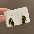 Close-up of dark green leaf stud earrings with gold edges on display card. - Black
