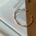 Detailed close-up of a gold wavy twisted open cuff bracelet on a minimalist background - Gold