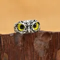 Vista macro dettagliata di un anello a gufo vintage con occhio di demone su legno - Occhio Giallo / Argento Antico