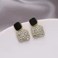Vista macro di eleganti orecchini a lobo quadrati dorati con smalto nero e strass lucidi - Black Drip Oil Gold Base / Diamante bianco