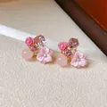 Primo piano di orecchini floreali rosa con rose e cristalli viola su nastro bianco. - Rosa