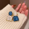 Primo piano di orecchini geometrici asimmetrici blu e crema con trama a increspatura d'acqua - Blu + Bianco