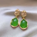 Primo piano di eleganti orecchini a goccia verdi con texture metallica dorata plissettata. - Verde