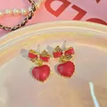 Close-up detail of red marble heart earrings with a crystal bow on an iridescent plate. - Red