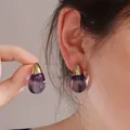 Dettaglio di orecchini minimalisti in resina oro e viola indossati su un orecchio di modella - Goccia d'Acqua Viola