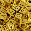 Macro detail of 6mm gold acrylic square alphabet letter beads for DIY jewelry making crafts - Gold Base with Black Text