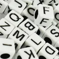 Macro view of 6mm white acrylic cubic alphabet beads with black printed letters - White Base Black Font