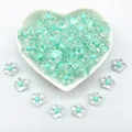 Detail view of 12mm clear acrylic flower beads with cyan centers in a heart dish - 12mm / Five-Petal Plum Blossom Style / 1000 Pieces/Pack / Green