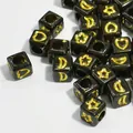 Close-up macro view of black 6mm acrylic cube beads with gold stars and moon patterns - 3000 Pieces/Pack / Black With Gold Text