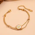 Detailansicht eines zweireihigen Gold-Titanstahl-Armbands mit weißem Herz-Anhänger-Detail. - Gold Doppellagiges Herz Armband