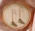 Gros plan détaillé de boucles d'oreilles pendantes en jade vert et perles rouges sur bois. - Boucles d'Oreilles Crochet Jade Grenat