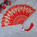 Primer plano de un elegante abanico plegable chino rojo con patrones de mariposas doradas. - Con borlas / Rojo
