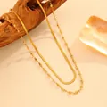 Vue en gros plan des détails de la chaîne serpent dorée double et du collier cœur perlé. - Collier double rang cœur doré, billes d'acier et maille plate