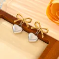 Detailed view of gold bow and silver heart pendant earrings in a wooden tray - Earrings Only / Gold + Silver (Two Tone)