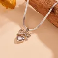 Detailopname van zilveren hartvormige hanger met strik aan een slanke slangenschakelketting. - Alleen Halsketting / Zilver