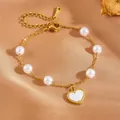 Detail van een gouden stalen armband met witte parels en een hartvormige hanger - Witte Schelp Hydraulisch Hart