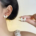 Detail view of French vintage white bow stud earrings worn on ear and held by hand. - Off-White Bowknot Style (EH3796)