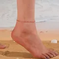 Gros plan d'un bracelet de cheville en cristal rose minimaliste sur une plage - Cristal Rose