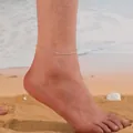 Vue détaillée d'une chevillère minimaliste en perles de cristal naturel portée à la plage. - Cristal Transparent