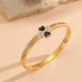 Gedetailleerde macro-weergave van gouden roestvrijstalen armband met klavermotief - Zwart-Wit Strass Klavertje Vier Stijl / Goud
