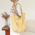 Large yellow and white striped canvas tote bag worn by a model in a cozy interior. - Yellow
