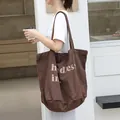 Bolso tote grande de lona marrón vintage con estampado de letras llevado por modelo - Café