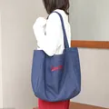 Bolso tote casual de mezclilla azul con bordado rojo Super Day lucido por una modelo. - Azul