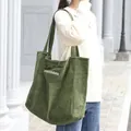 Green corduroy tote bag with white letter embroidery in a casual outdoor setting. - Green