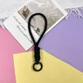 Macro view of a black braided paracord wrist strap with a matte black metal ring. - Phone Cord / 1 Piece / Black